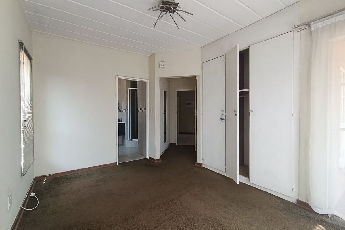 Spacious bedroom featuring built-in cupboards, carpeted flooring, and direct access to an en-suite bathroom.