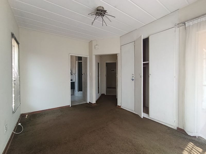 Spacious bedroom featuring built-in cupboards, carpeted flooring, and direct access to an en-suite bathroom.