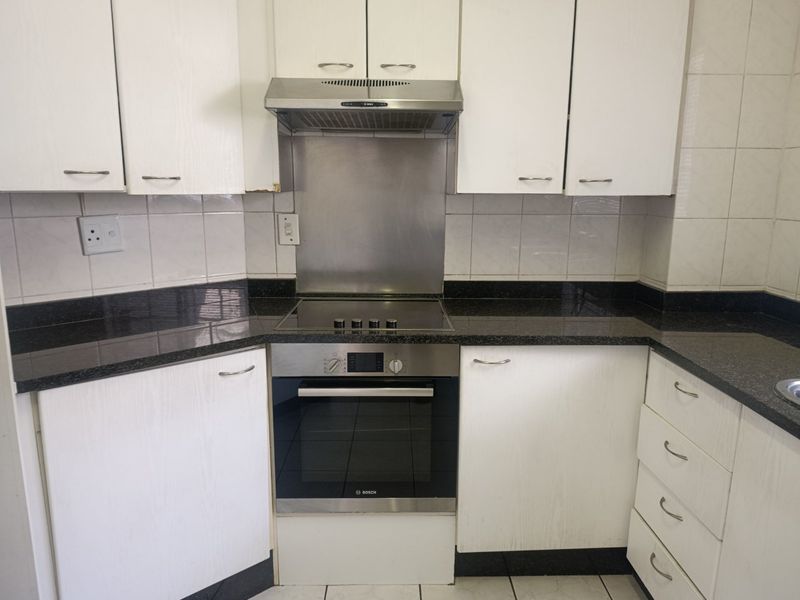 A functional kitchen featuring white cabinetry, dark granite countertops, a stainless steel extractor fan, and a built-in electric oven and hob.