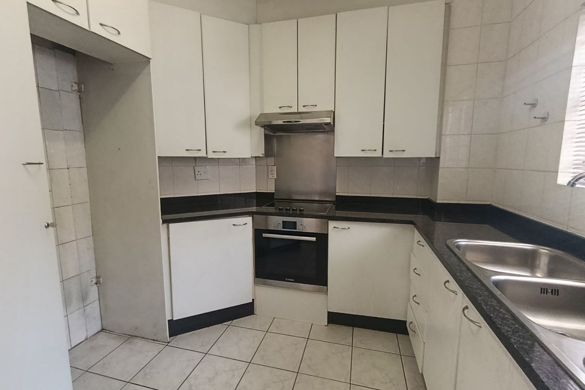 A functional kitchen featuring white built-in cabinetry, granite countertops, a stainless steel double sink, and integrated oven with extractor fan.