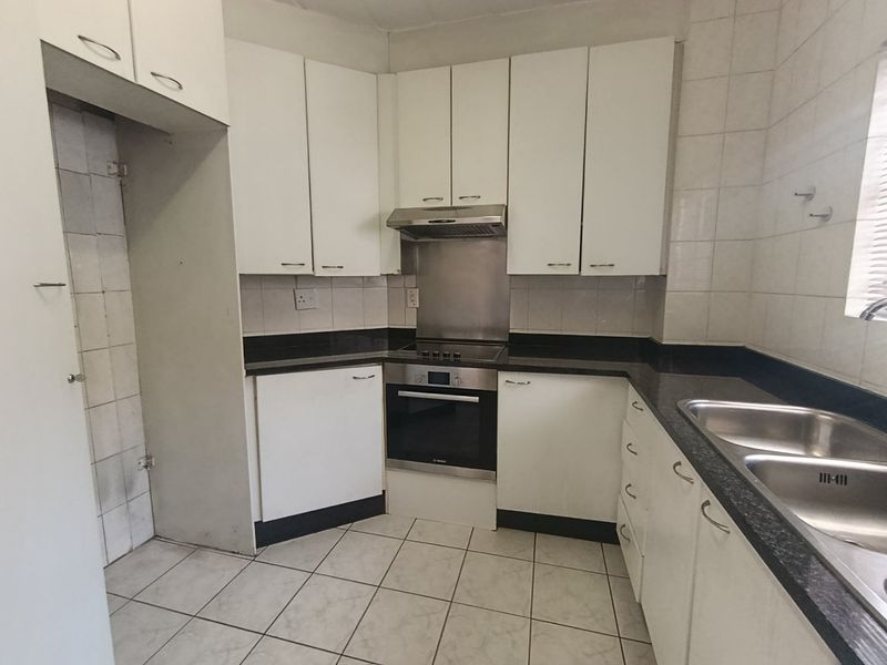 A functional kitchen featuring white built-in cabinetry, granite countertops, a stainless steel double sink, and integrated oven with extractor fan.