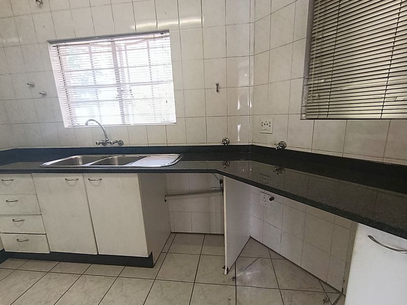 A functional kitchen space featuring granite countertops, double basin sink, and tiled finishes, currently vacant and ready for renovation or modernization.