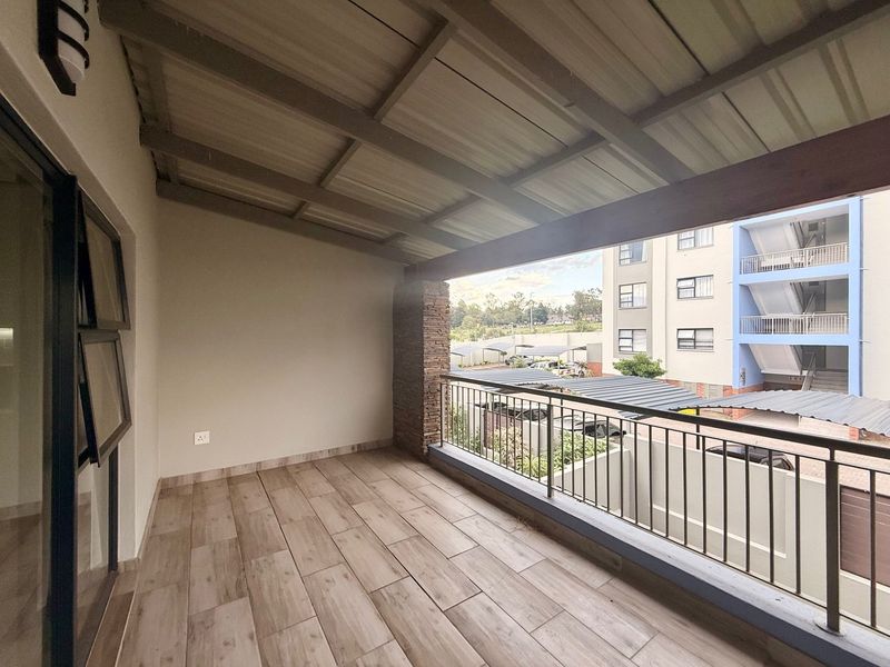 A covered balcony featuring wood-look tiled flooring, a stone-clad pillar, and metal railings, offering an open outdoor space.