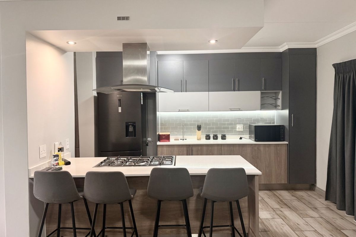 Modern kitchen featuring two-tone cabinetry, stone countertops, a central island with a gas hob, and integrated lighting for a sleek, functional workspace.