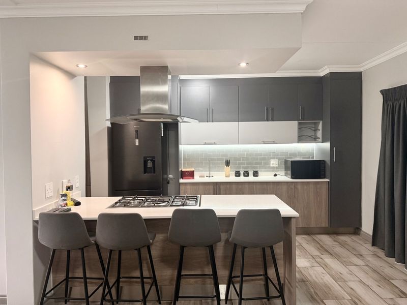 Modern kitchen featuring two-tone cabinetry, stone countertops, a central island with a gas hob, and integrated lighting for a sleek, functional workspace.