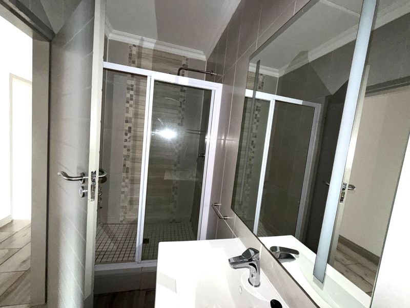 A modern bathroom featuring a glass-enclosed shower, a vanity basin with a mixer tap, and a large wall-mounted mirror with neutral tiling.