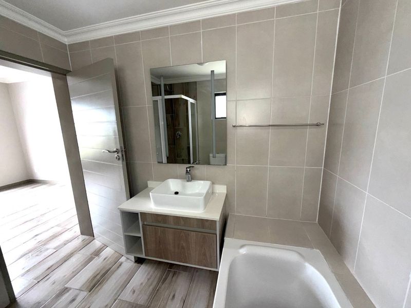 A modern bathroom featuring a vessel sink on a wood-finish vanity, a built-in bathtub, and neutral wall tiling.