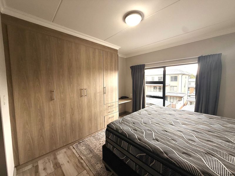 A well-maintained bedroom featuring extensive built-in wooden cabinetry, a integrated desk area, and modern laminate flooring with natural light.