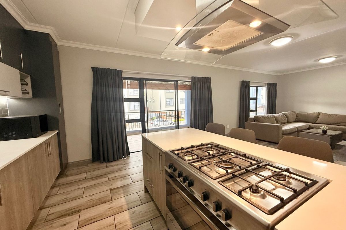 Modern open-plan kitchen and living area featuring a central island with gas hob, sleek cabinetry, and direct access to a balcony through sliding doors.