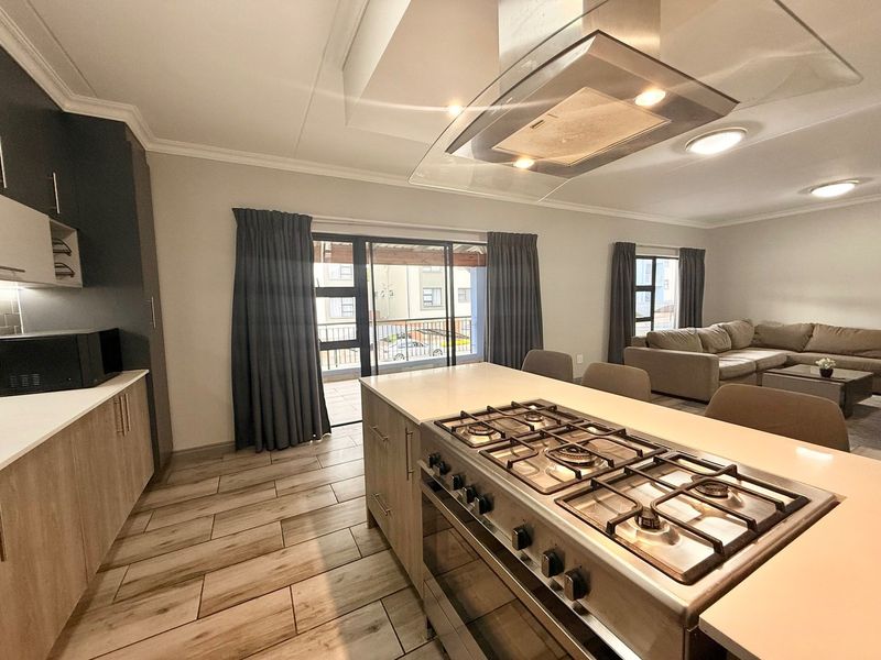 Modern open-plan kitchen and living area featuring a central island with gas hob, sleek cabinetry, and direct access to a balcony through sliding doors.