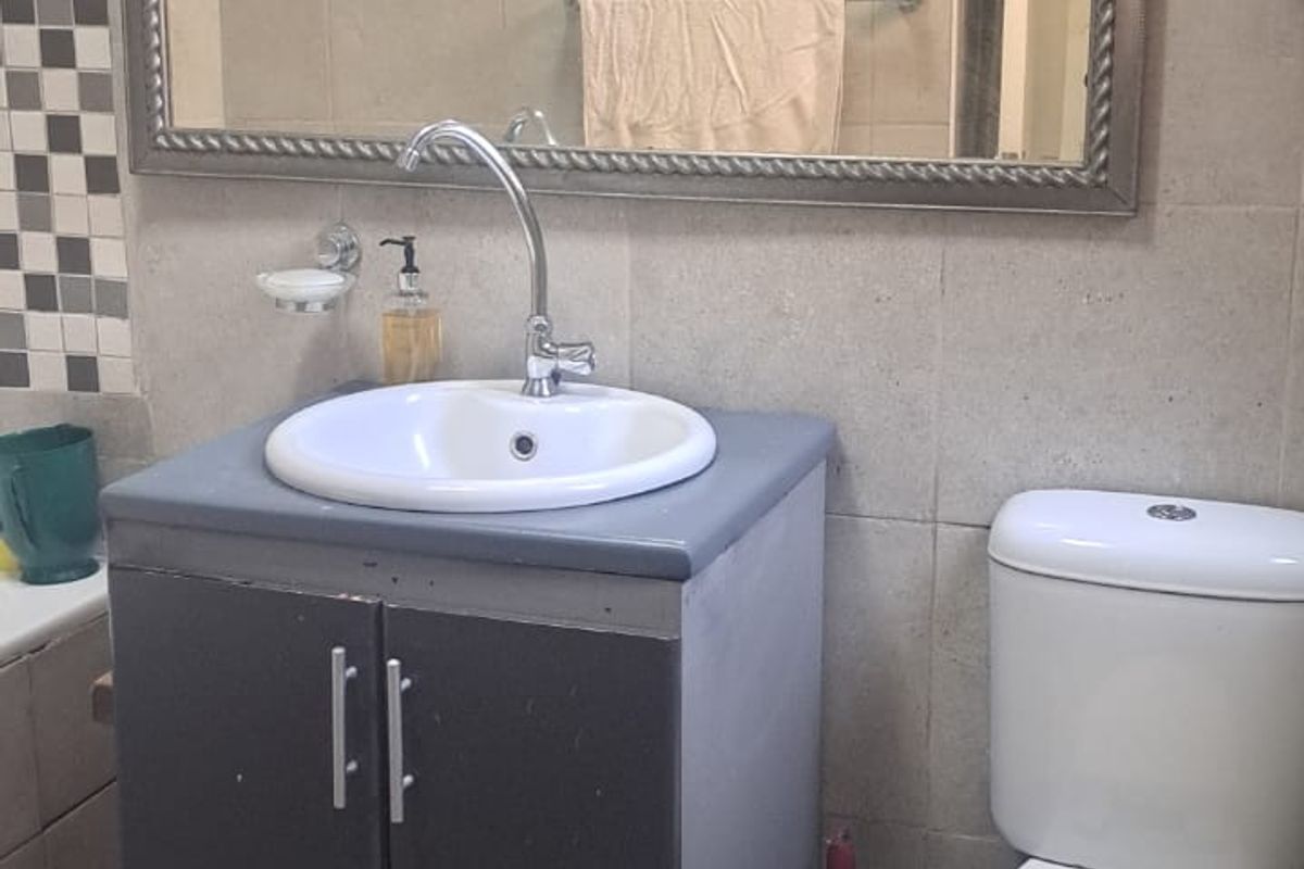 A functional bathroom featuring a vanity cabinet with a ceramic basin, chrome faucet, wall-mounted mirror, and a standard toilet with tiled finishes.