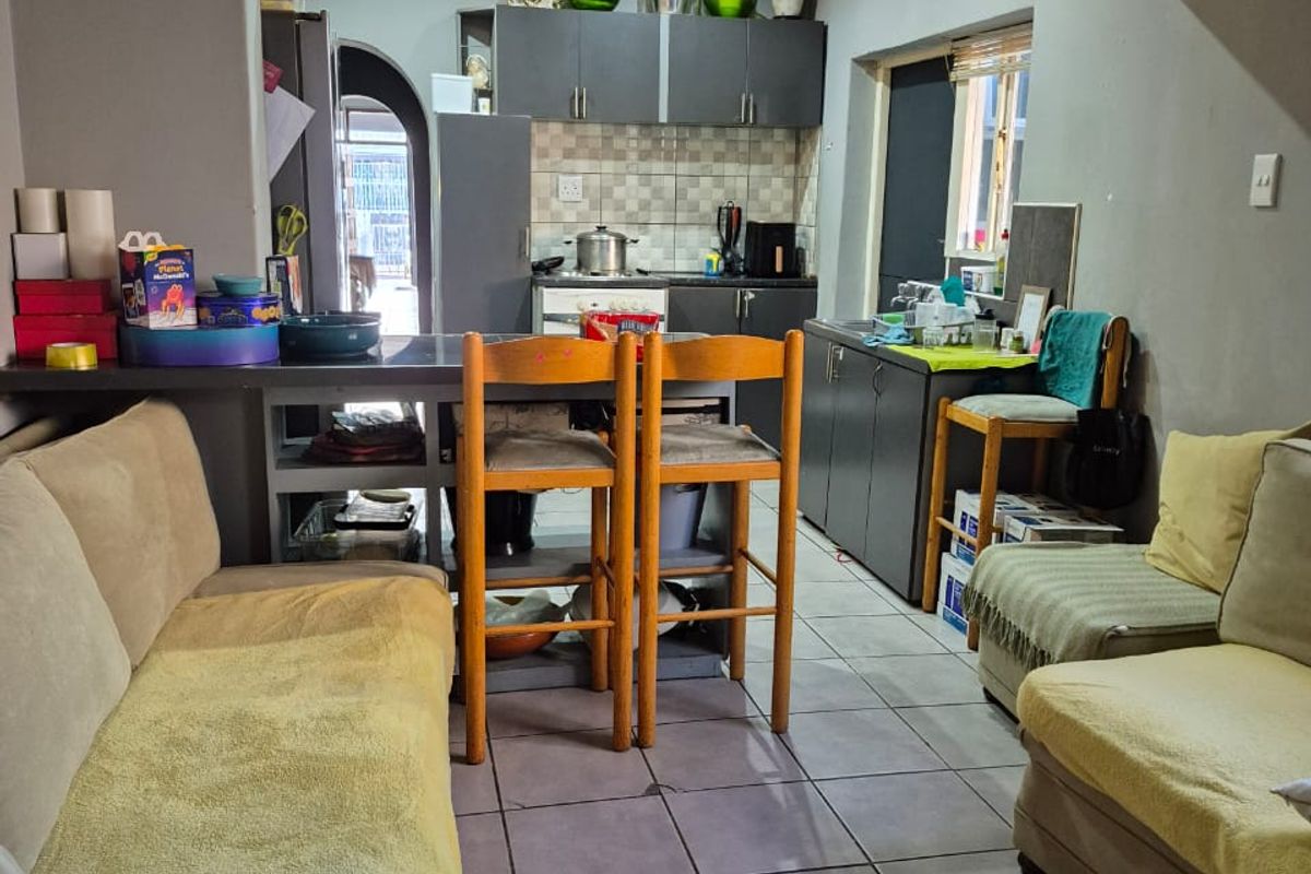 Open-plan living and kitchen area featuring tiled flooring, a breakfast bar, and built-in cabinetry, offering a functional layout with potential for cosmetic updates.