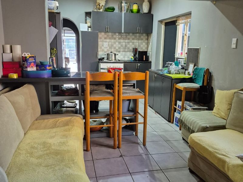 Open-plan living and kitchen area featuring tiled flooring, a breakfast bar, and built-in cabinetry, offering a functional layout with potential for cosmetic updates.