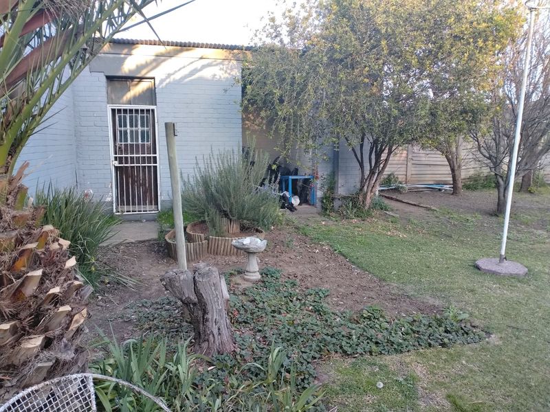 Rear exterior view of the property featuring a brick facade, security gate, and a garden area requiring landscaping and maintenance.