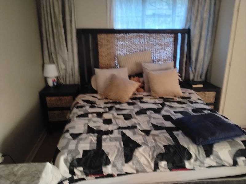 A bedroom featuring a bed with a woven headboard and curtains framing the window.
