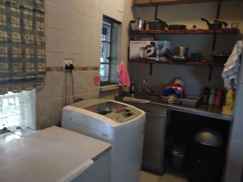 A functional laundry area featuring a stainless steel sink, wall-mounted shelving, and tiled splashback, providing practical utility space.