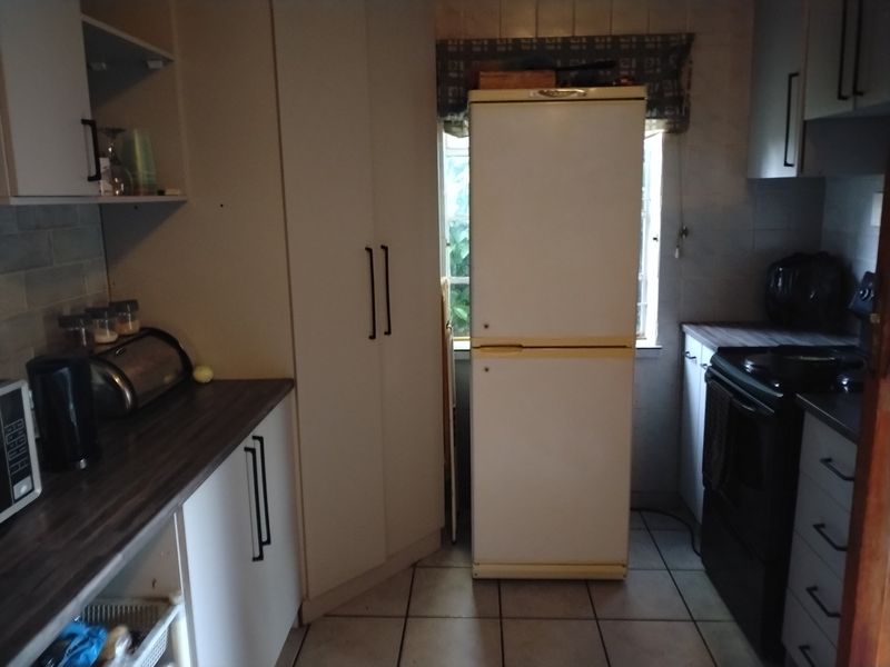 A functional kitchen featuring tiled flooring, laminate countertops, and built-in cabinetry with a tiled backsplash.