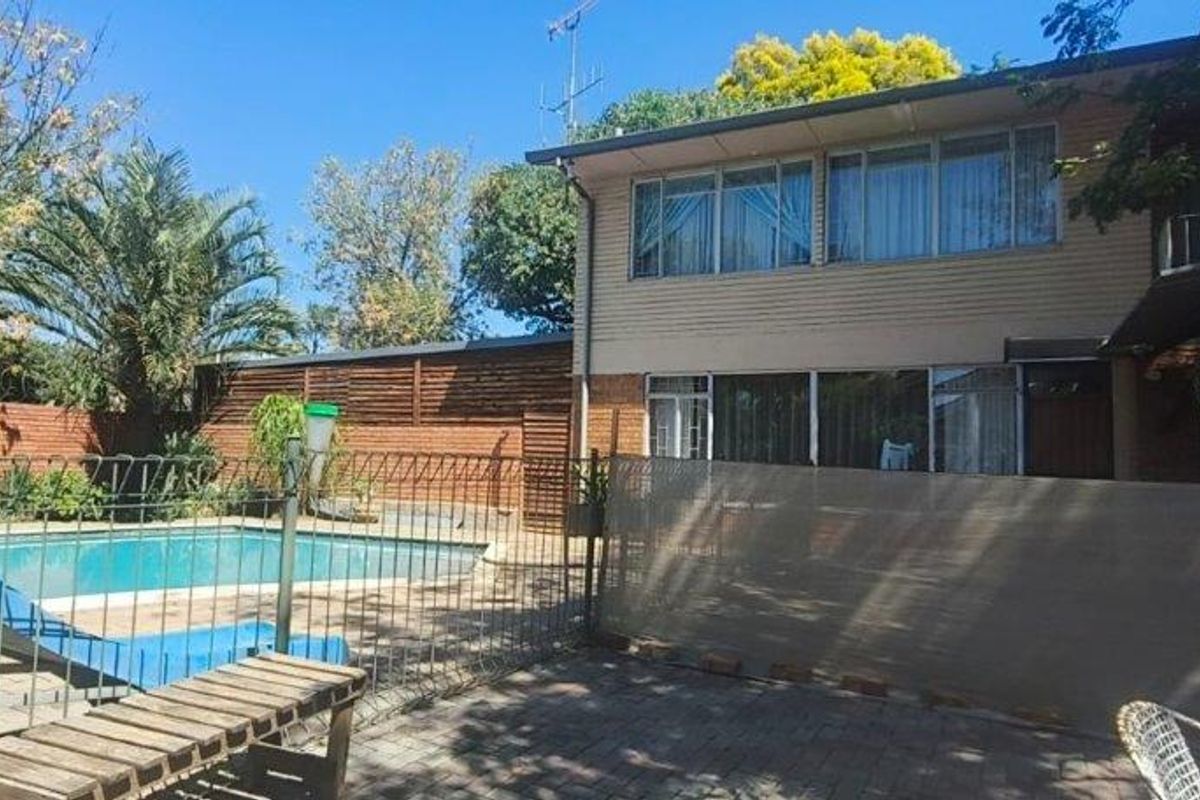 Rear exterior view of a two-story house featuring a swimming pool, paved patio area, and established garden surroundings.