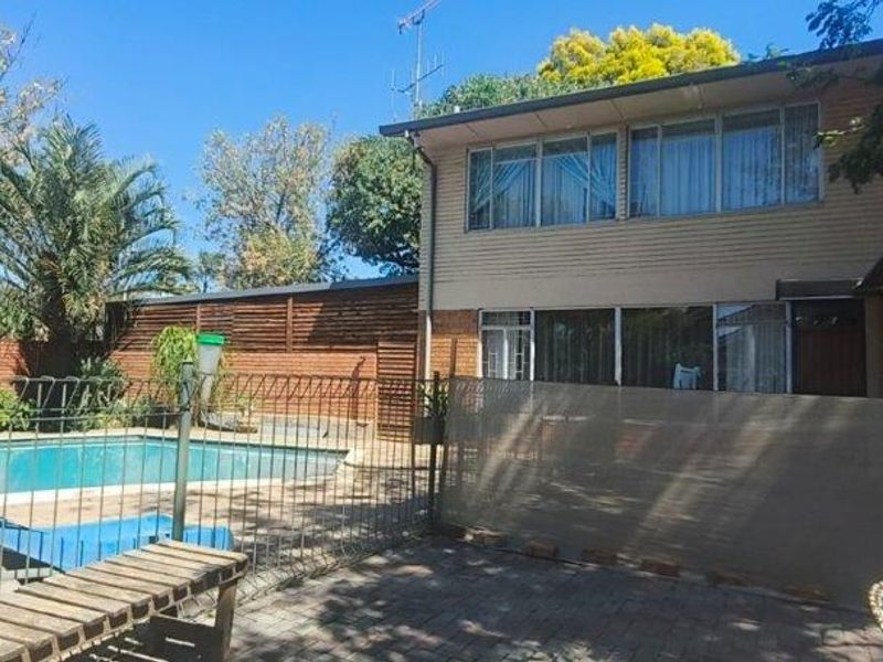 Rear exterior view of a two-story house featuring a swimming pool, paved patio area, and established garden surroundings.