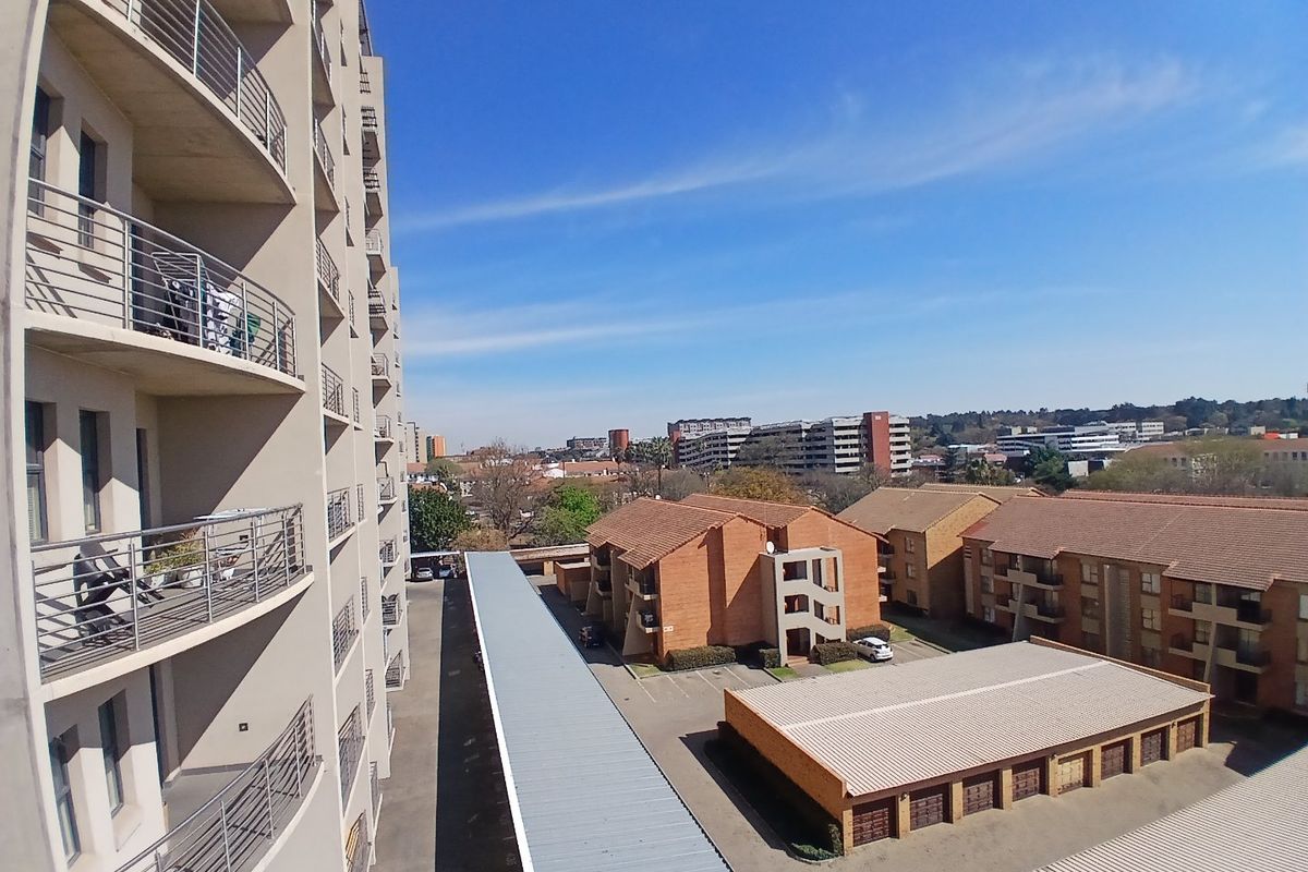 An elevated aerial view of the apartment complex, showcasing the building facade, balconies, surrounding parking structures, and neighborhood landscape.