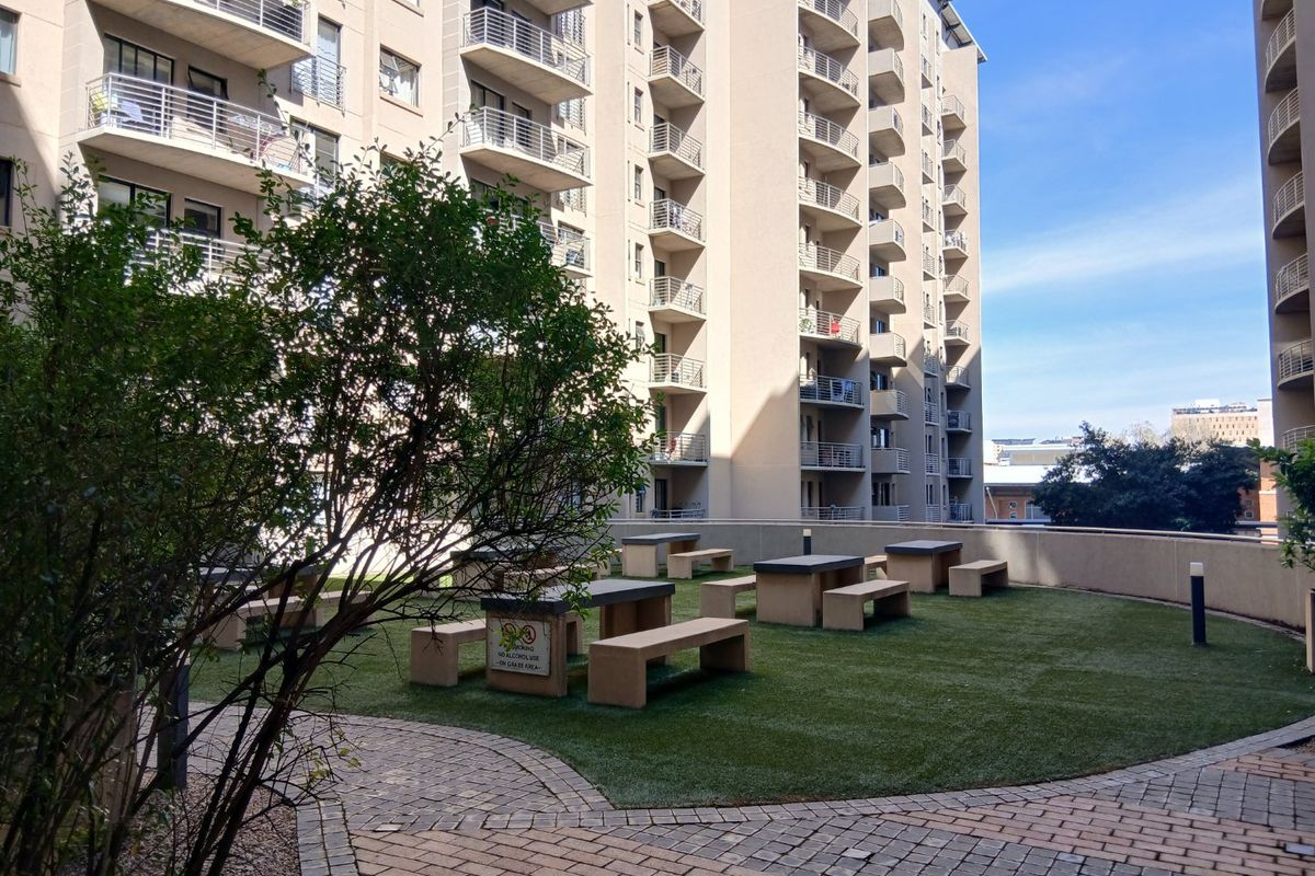 A communal outdoor garden area featuring artificial turf, paved pathways, and fixed concrete seating, situated between apartment building blocks.