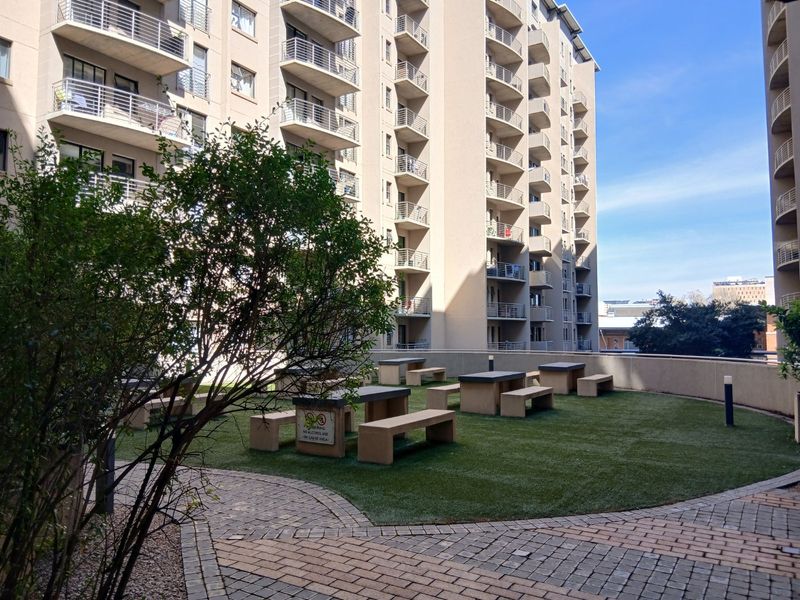 A communal outdoor garden area featuring artificial turf, paved pathways, and fixed concrete seating, situated between apartment building blocks.