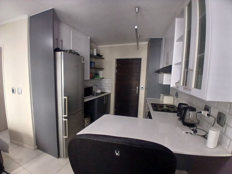 A modern kitchen featuring white and grey cabinetry, a subway tile backsplash, a built-in hob with extractor, and a functional breakfast bar area.