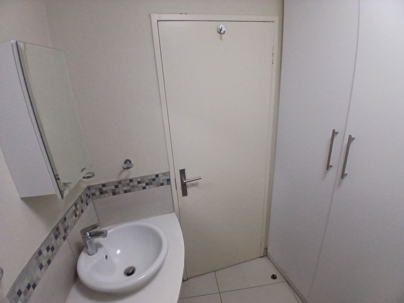A functional bathroom featuring a vanity basin with a mixer tap, tiled splashback, and built-in storage cupboards.
