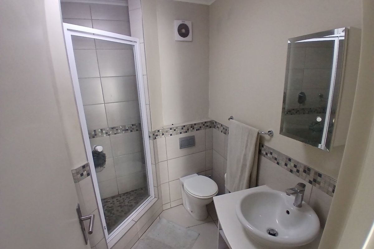 A functional bathroom featuring a shower enclosure, toilet, and vanity basin with a wall-mounted mirror and tiled accents.