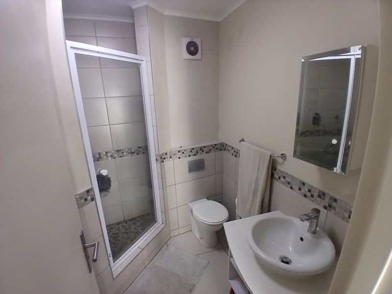 A functional bathroom featuring a shower enclosure, toilet, and vanity basin with a wall-mounted mirror and tiled accents.
