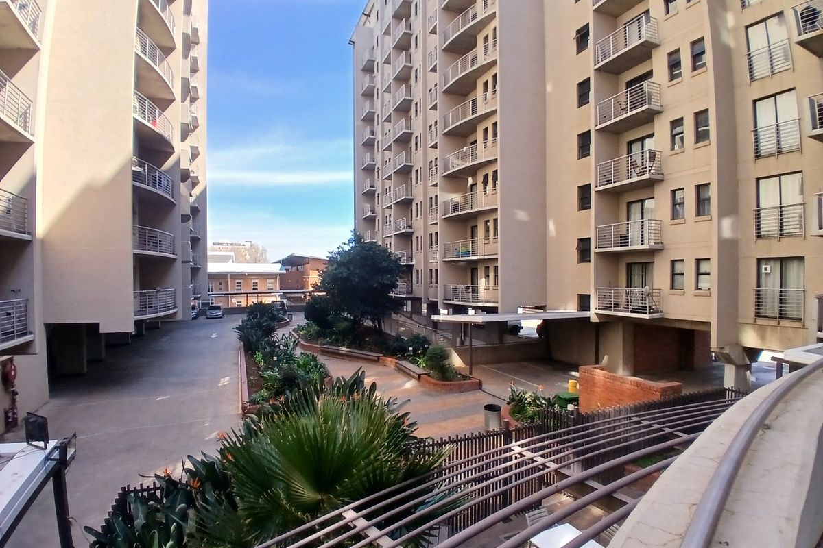 View of the apartment complex courtyard featuring landscaped gardens, paved driveway, and multiple levels of private balconies.