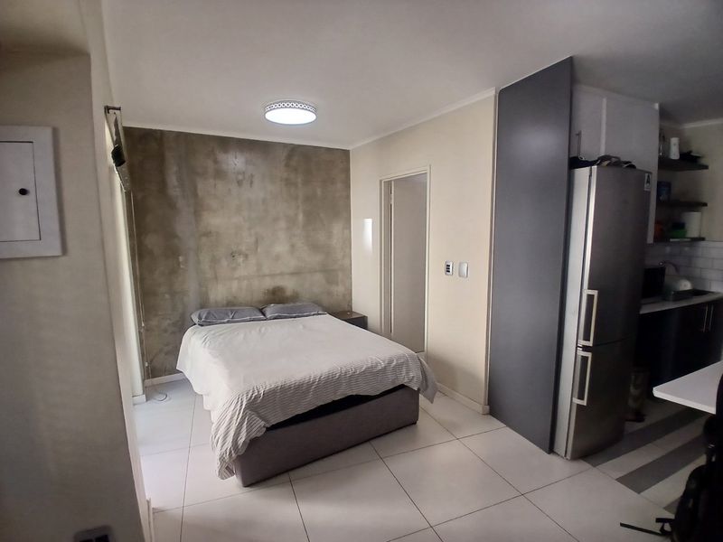 An open-plan studio apartment featuring tiled flooring, an exposed concrete feature wall, and a compact kitchen area with built-in cabinetry.