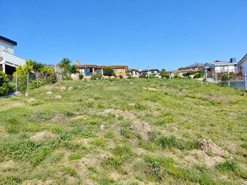A vacant residential plot featuring a sloped landscape with established boundary fencing, situated in a developed neighborhood setting.