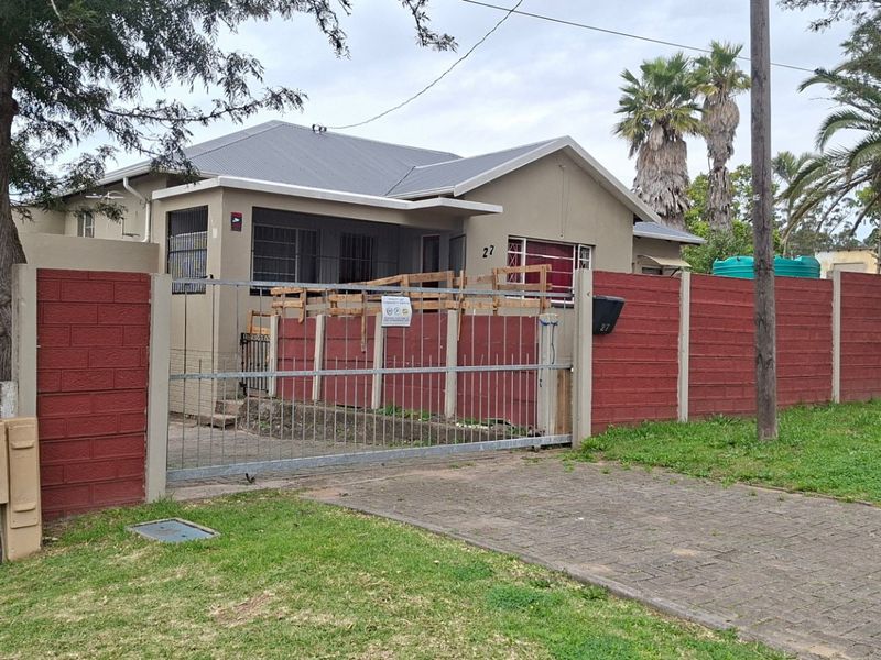 Front exterior view of a residential property featuring a paved driveway, metal sliding gate, and a precast concrete boundary wall.