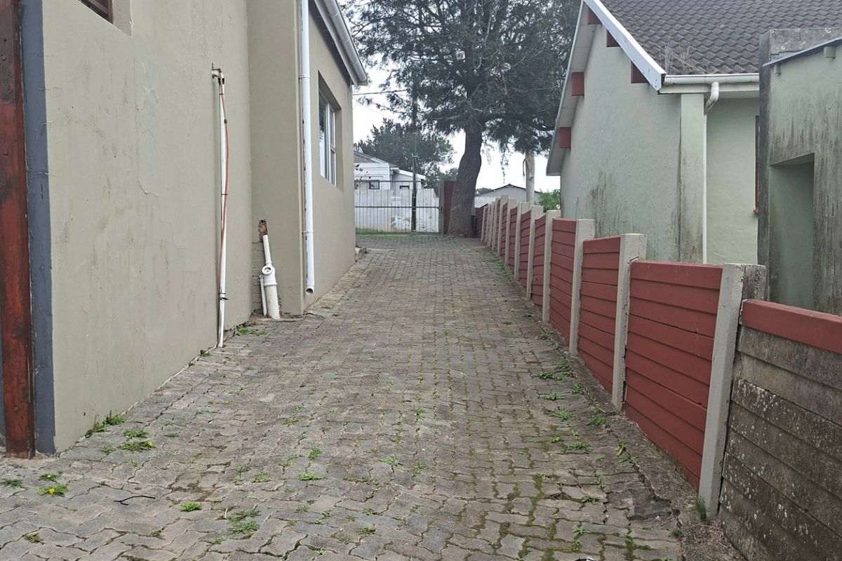 A narrow paved side passage between two residential structures, featuring a precast concrete boundary wall and external plumbing fixtures.