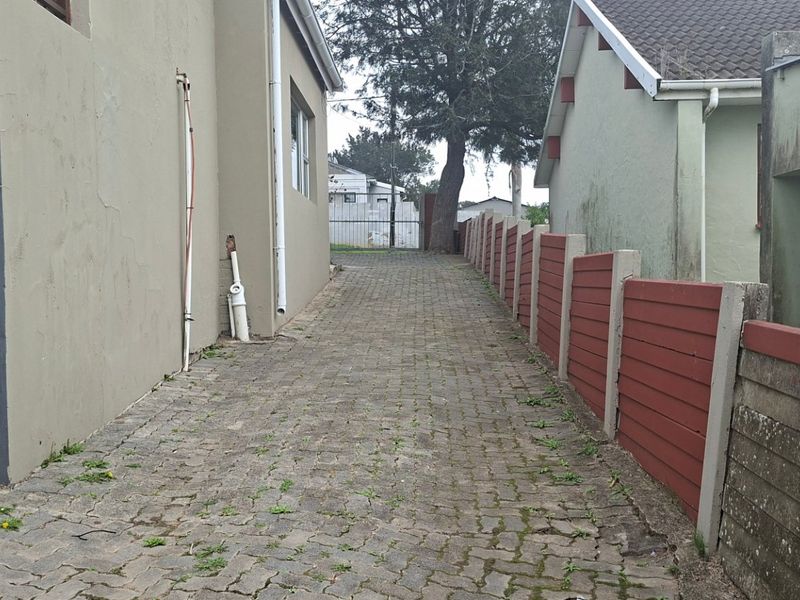 A narrow paved side passage between two residential structures, featuring a precast concrete boundary wall and external plumbing fixtures.