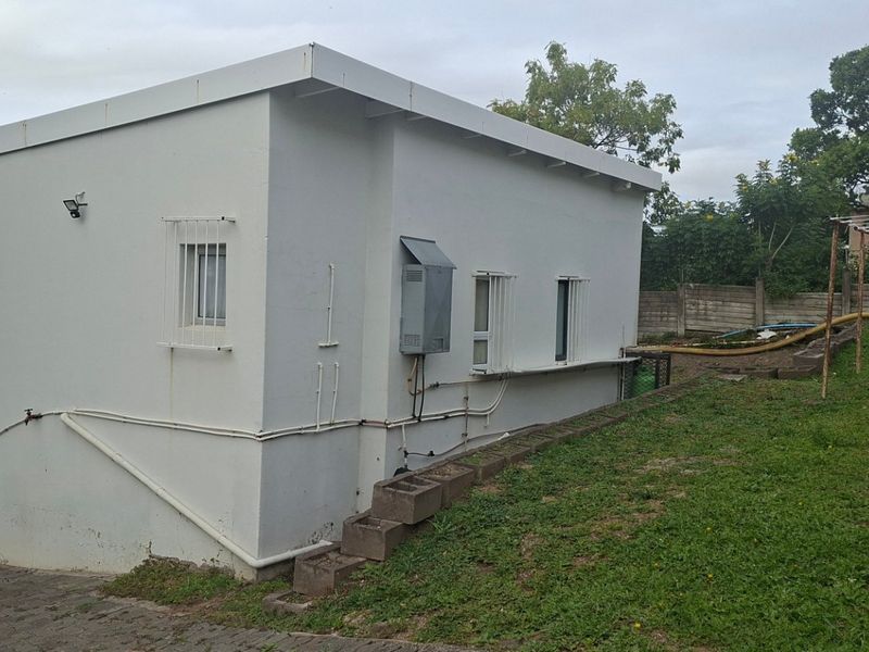 Rear view of the property showing the exterior wall, security bars, external electrical box, and paved driveway area.