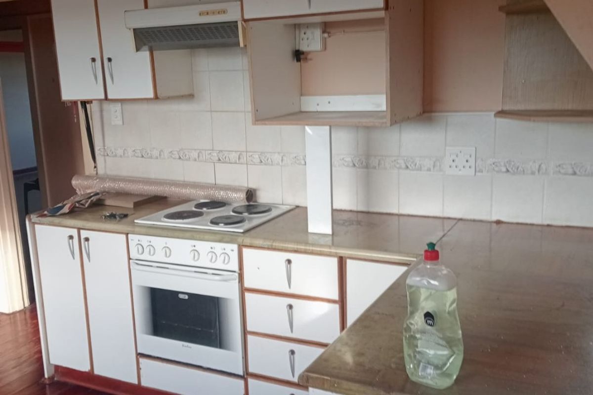 A dated kitchen featuring white cabinetry, an integrated electric oven and hob, tiled backsplash, and timber flooring, offering potential for a modern renovation.