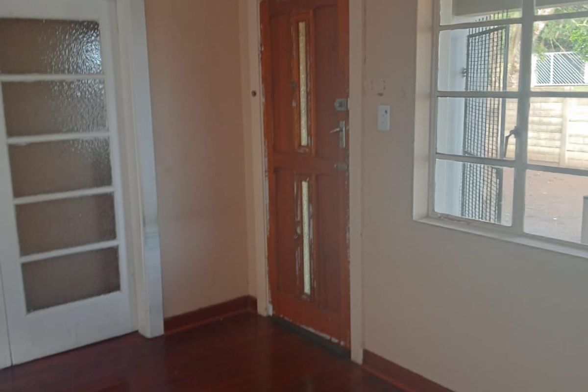 An empty living area featuring polished timber flooring, a classic glass-panelled door, and a steel-framed window looking out to the exterior.