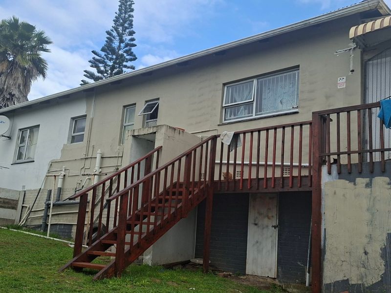 Rear exterior view of the house featuring a wooden staircase leading to a deck, with visible signs of exterior wear and maintenance requirements.