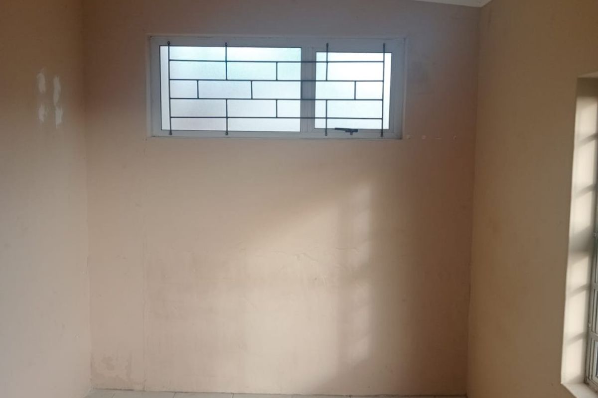 An empty bedroom featuring tiled flooring, coved ceilings, and windows fitted with security bars.