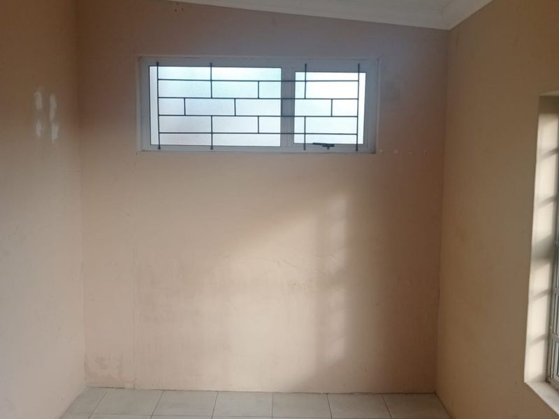An empty bedroom featuring tiled flooring, coved ceilings, and windows fitted with security bars.