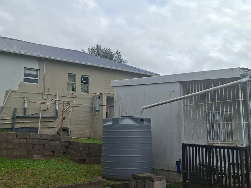 Rear view of the property featuring a water storage tank, rainwater harvesting system, and security bars on the windows.