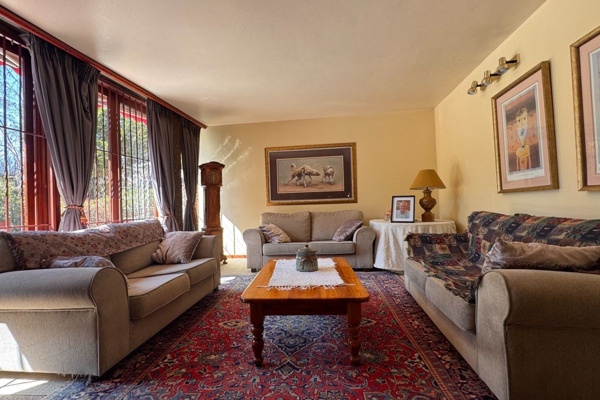 A spacious living room featuring large windows with security bars, providing ample natural light and a view of the outdoor area.