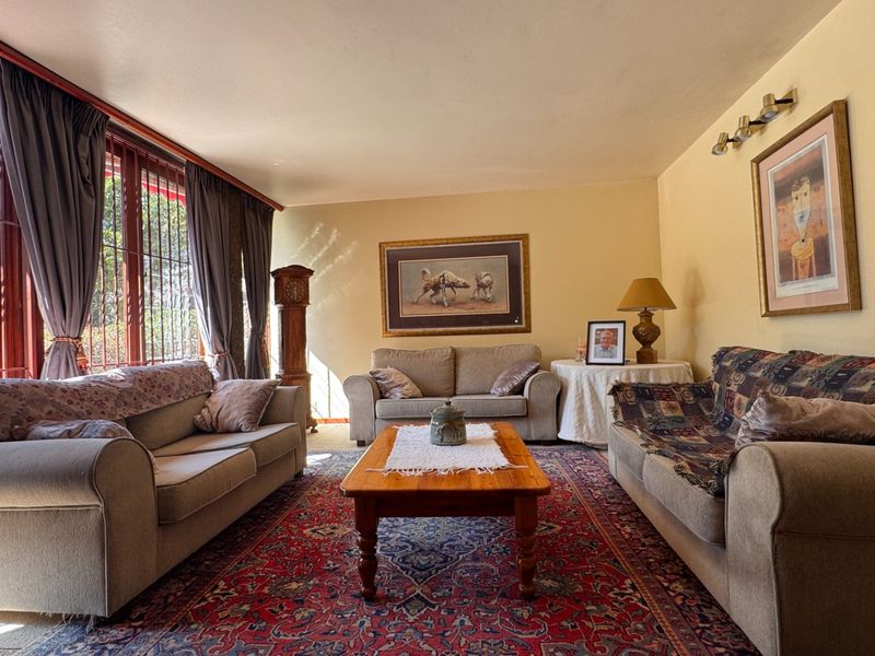 A spacious living room featuring large windows with security bars, providing ample natural light and a view of the outdoor area.