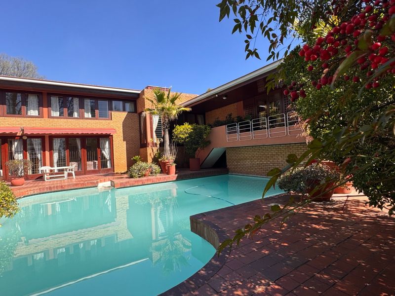 A spacious outdoor pool area featuring brick paving, a swimming pool, and a multi-level brick residence with a balcony and staircase.