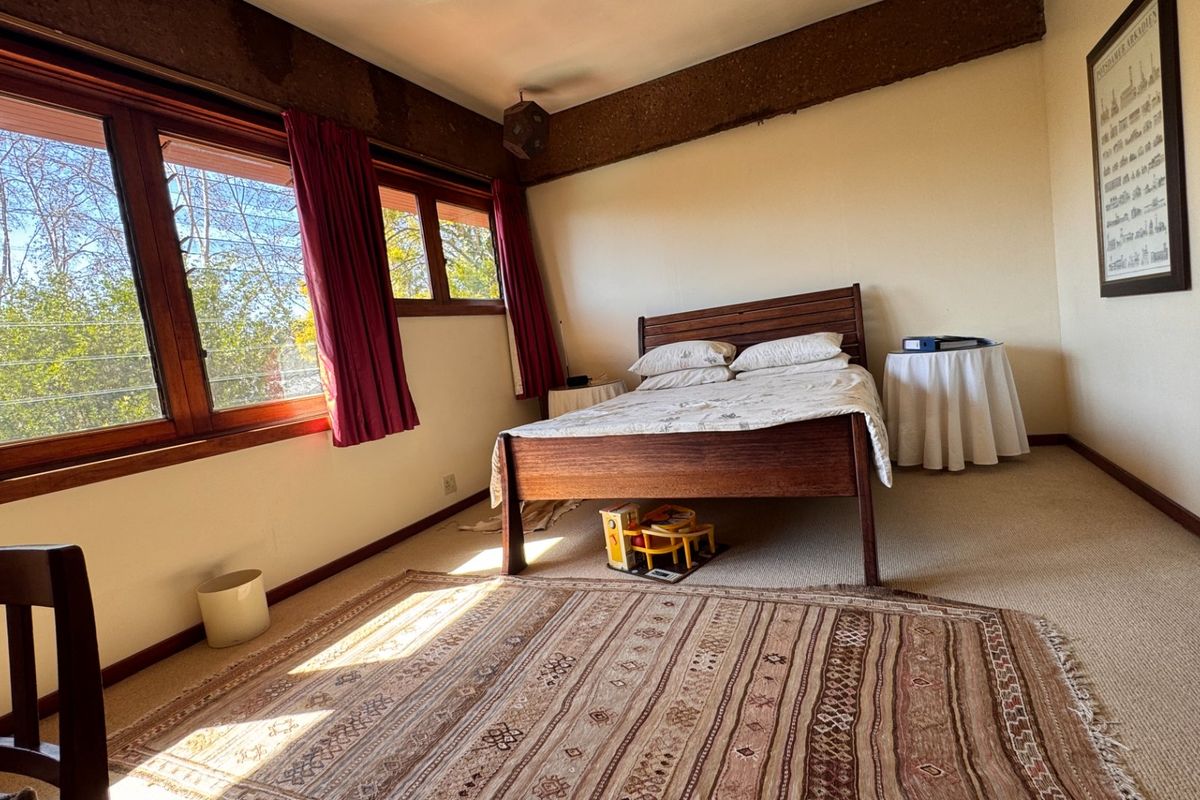A bedroom featuring timber-framed windows, an exposed ceiling beam, and carpeted flooring, offering a functional space with natural light.