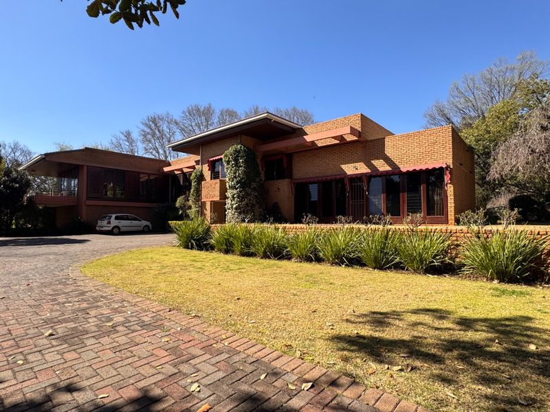 A well-maintained brick house featuring a spacious paved driveway, established garden, and classic architectural design with timber window frames.