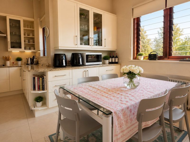 A well-maintained kitchen featuring cream cabinetry, granite countertops, stainless steel extractor fan, and tiled flooring, with an integrated dining area and natural light.