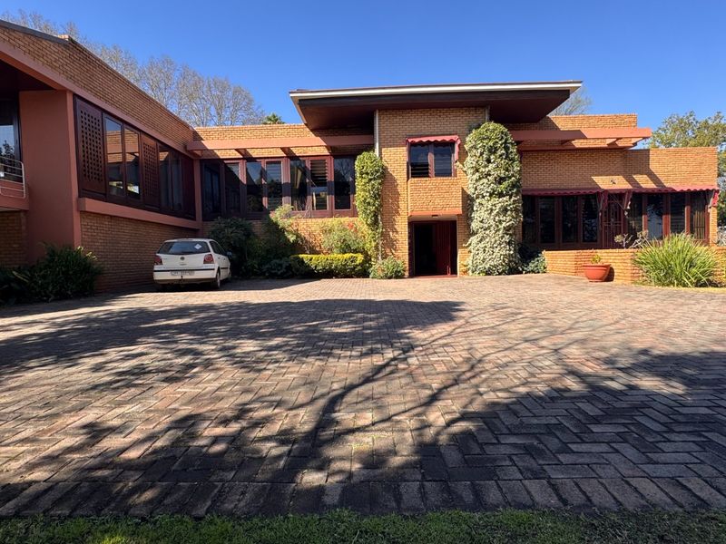 A spacious front exterior view of a brick house featuring a large paved driveway and a covered entrance with established landscaping.